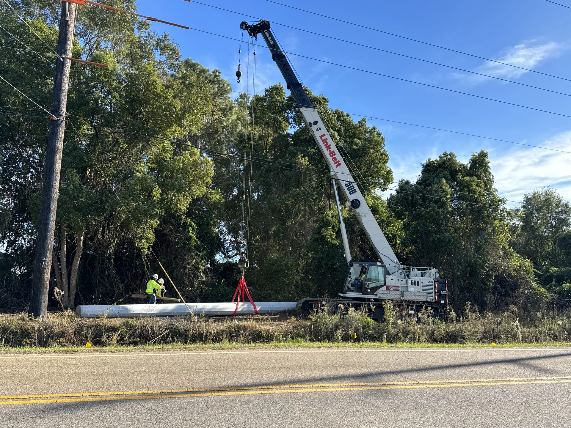 Crew and crane preparing a steel transmission pole along an existing right-of-way.