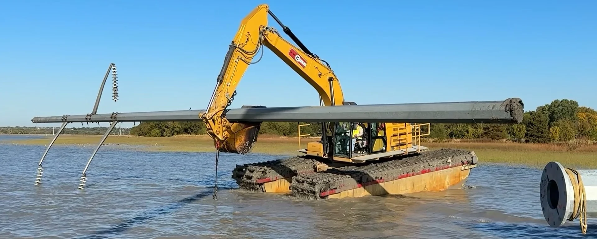 Amphibious equipment transporting a pole through water.