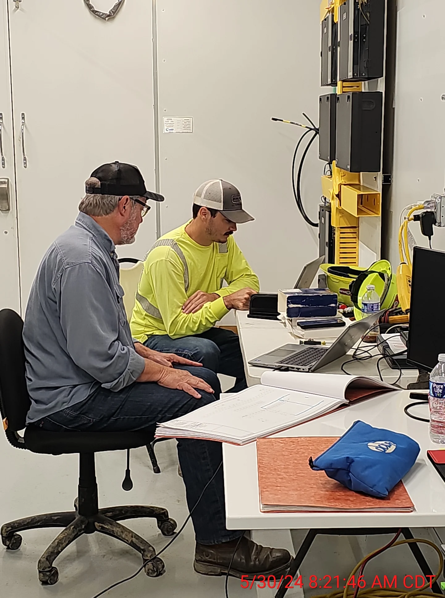 Testing and commissioning personnel reviewing drawings in a substation control house.